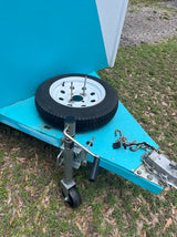 This teal RV rental trailer features a front-mounted spare tire, hitch, and jack, ready for your trip.