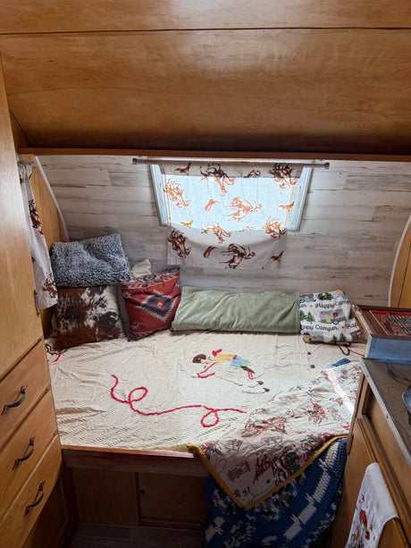 Cozy RV rental interior with western-themed bedding, a bed, and wooden cabinetry, creating a comfortable travel space.