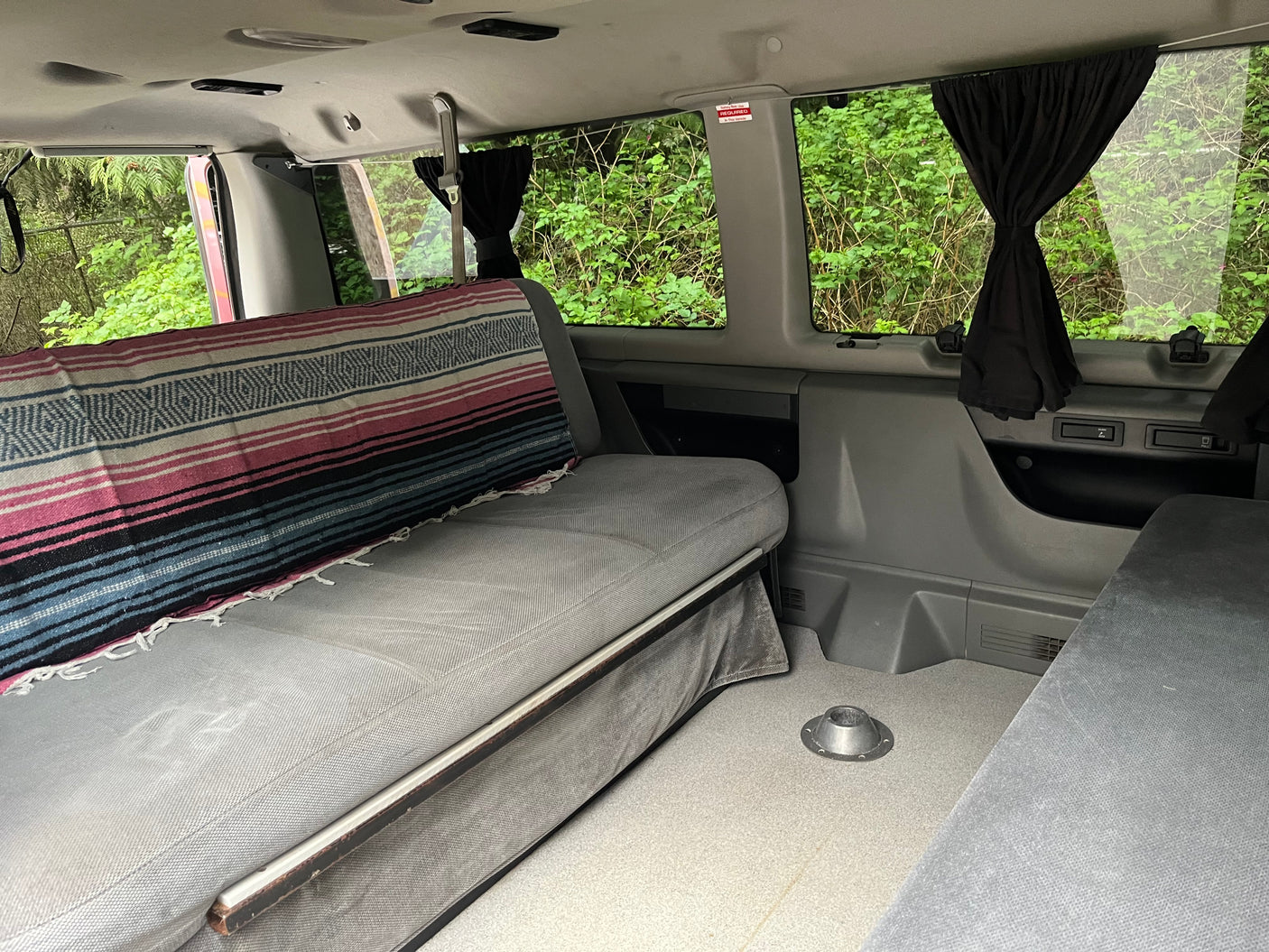 Comfortable RV rental van interior featuring a versatile bench seat with a vibrant blanket, curtained windows, and a floor table base.
