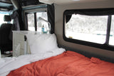 Cozy RV rental interior with a bed, small kitchen sink area, and scenic snowy landscape visible through the windows.