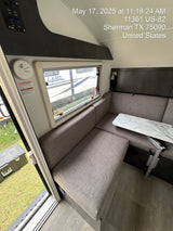 Compact RV rental interior: dinette with table & bench seating, window view, smoke alarm, and control panel.