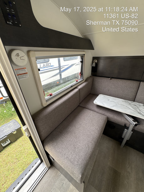 Compact RV rental interior: dinette with table & bench seating, window view, smoke alarm, and control panel.