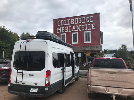 White Ford Transit RV rental parked at the rustic Polebridge Mercantile, a general store with bakery & pizza.