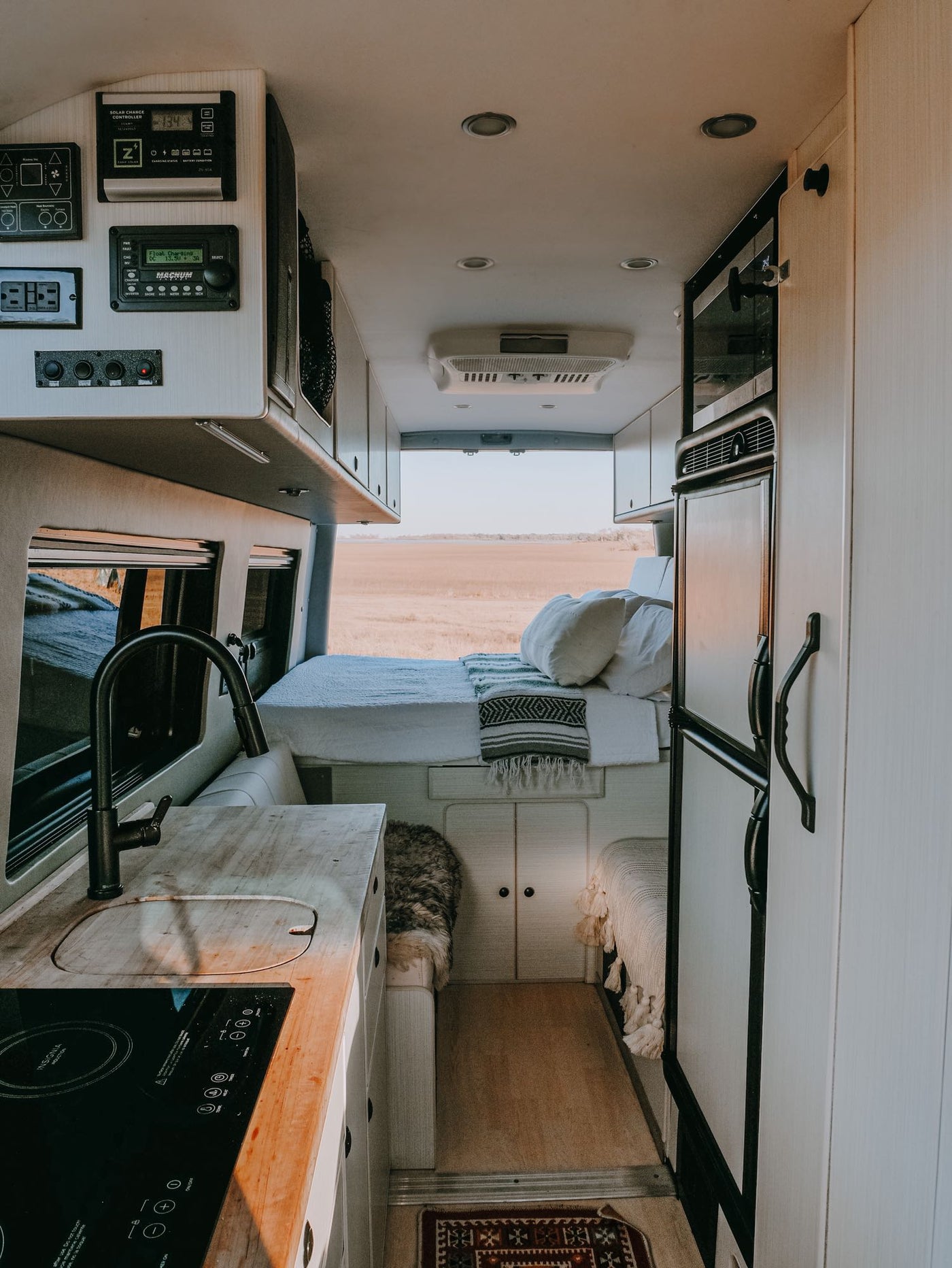  parked by a lake with vibrant bluebonnet flowers in the foreground.|Red RV rental van at Prada Marfa desert art installation. Driver waves from the window.|This RV rental shows a modern camper van interior: kitchen — photo 2