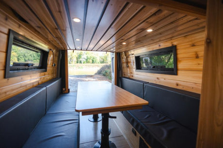 Experience comfort in this RV rental's wood interior: cozy benches, dining table, and nature views.