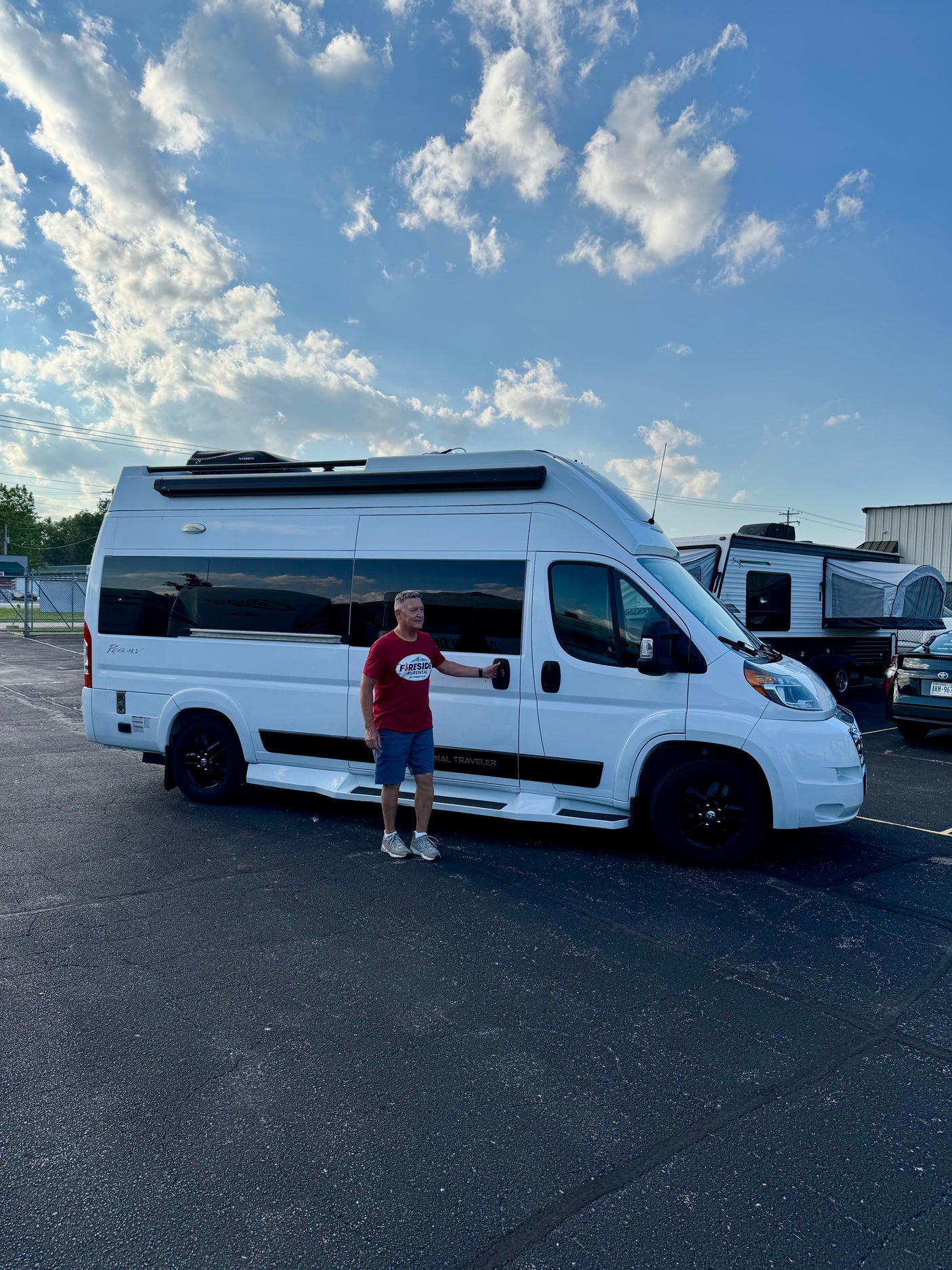 Man poses with a white camper van from Fireside RV Rental, ready for a travel adventure under a cloudy sky.