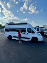 Man poses with a white camper van from Fireside RV Rental, ready for a travel adventure under a cloudy sky.