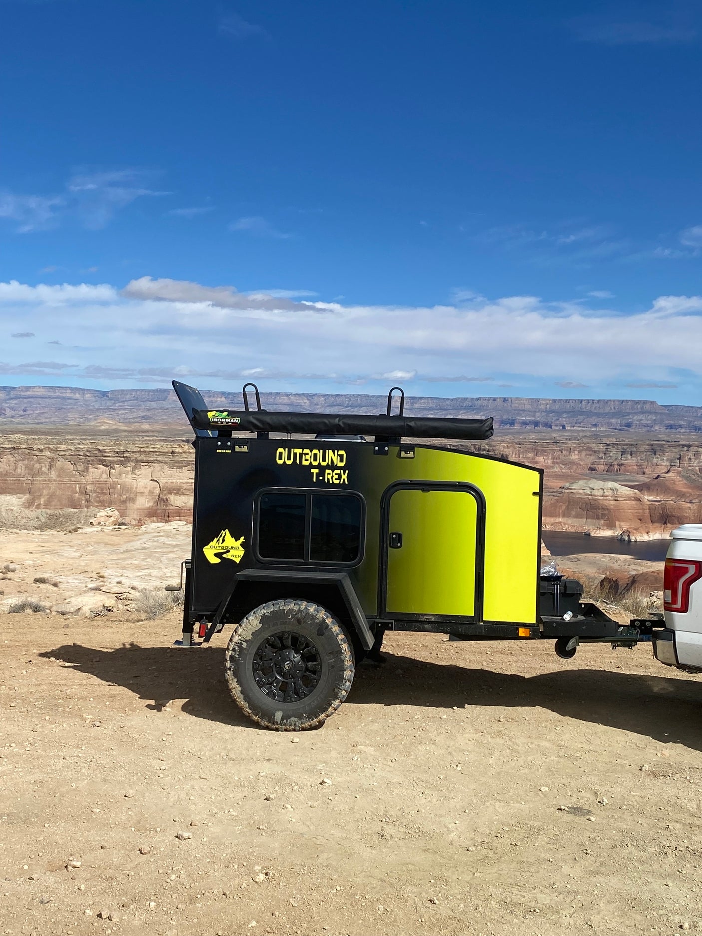 Outbound T-Rex overland trailer (black/lime), a rugged RV rental, overlooks a vast desert canyon with layered rock formations.