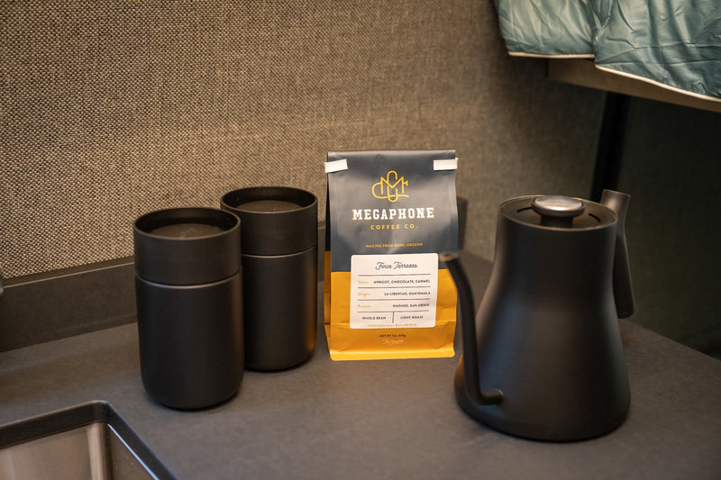 Compact coffee station in an RV rental, featuring Megaphone Coffee beans, a kettle, and two black tumblers. — photo 11
