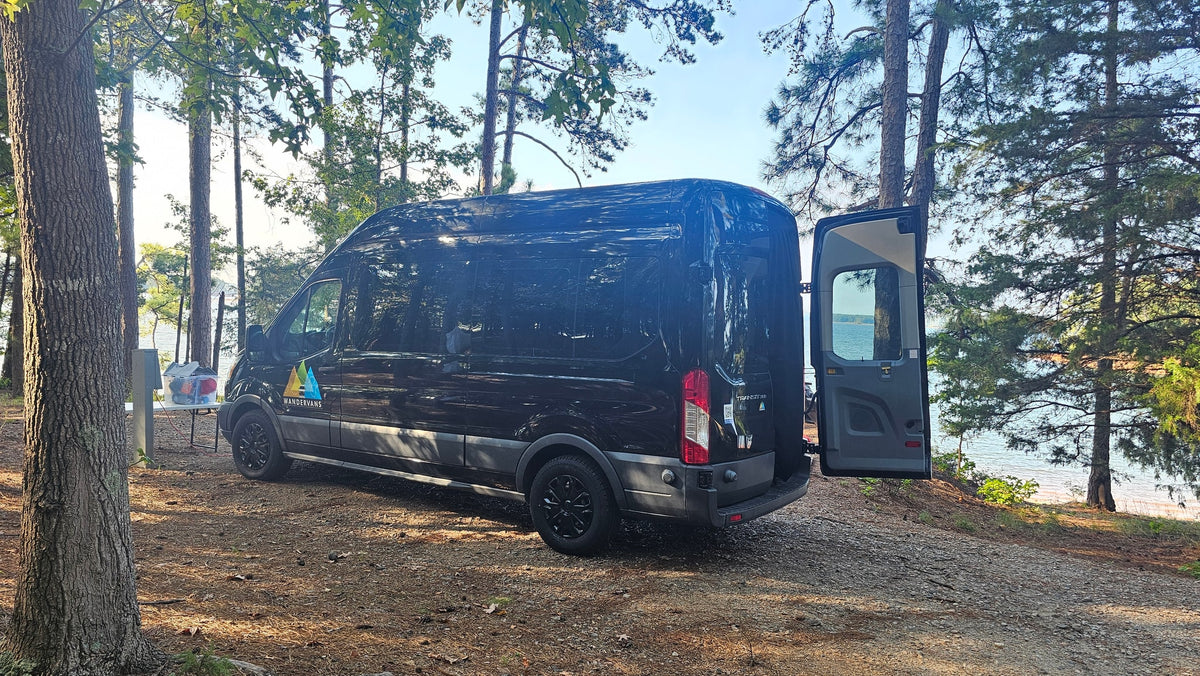 Black RV rental van at a shaded lakeside campsite. Rear doors open