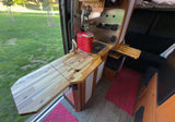 RV rental camper van kitchen: wooden counter with sink, red coffee maker, extendable counter, & view of green grass.