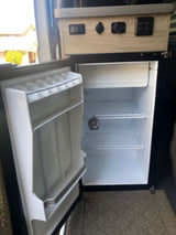 An RV rental's compact interior kitchen area, featuring an open mini-fridge and convenient power outlets.