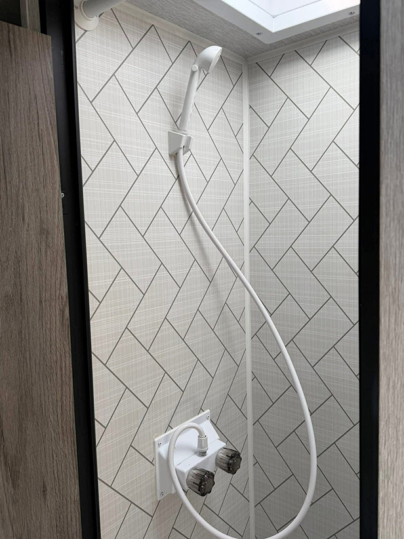 This clean, modern shower in an RV rental features light grey geometric patterned walls and a white handheld shower. — photo 11