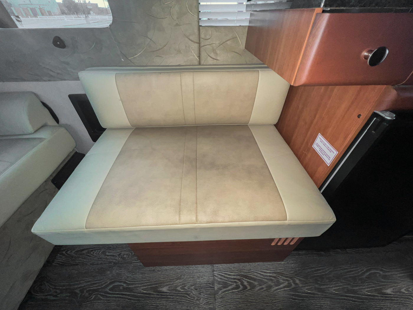 RV rental interior: A beige and white upholstered bench seat, with wood paneling, dark flooring, and a window. — photo 16