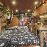 Inside this charming RV rental: a floral bed, compact kitchen, and warm wooden interior with string lights for cozy travel.