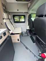 RV rental interior: light quilted rear seats, black front seats, and a functional side counter with fridge. Ready for travel.