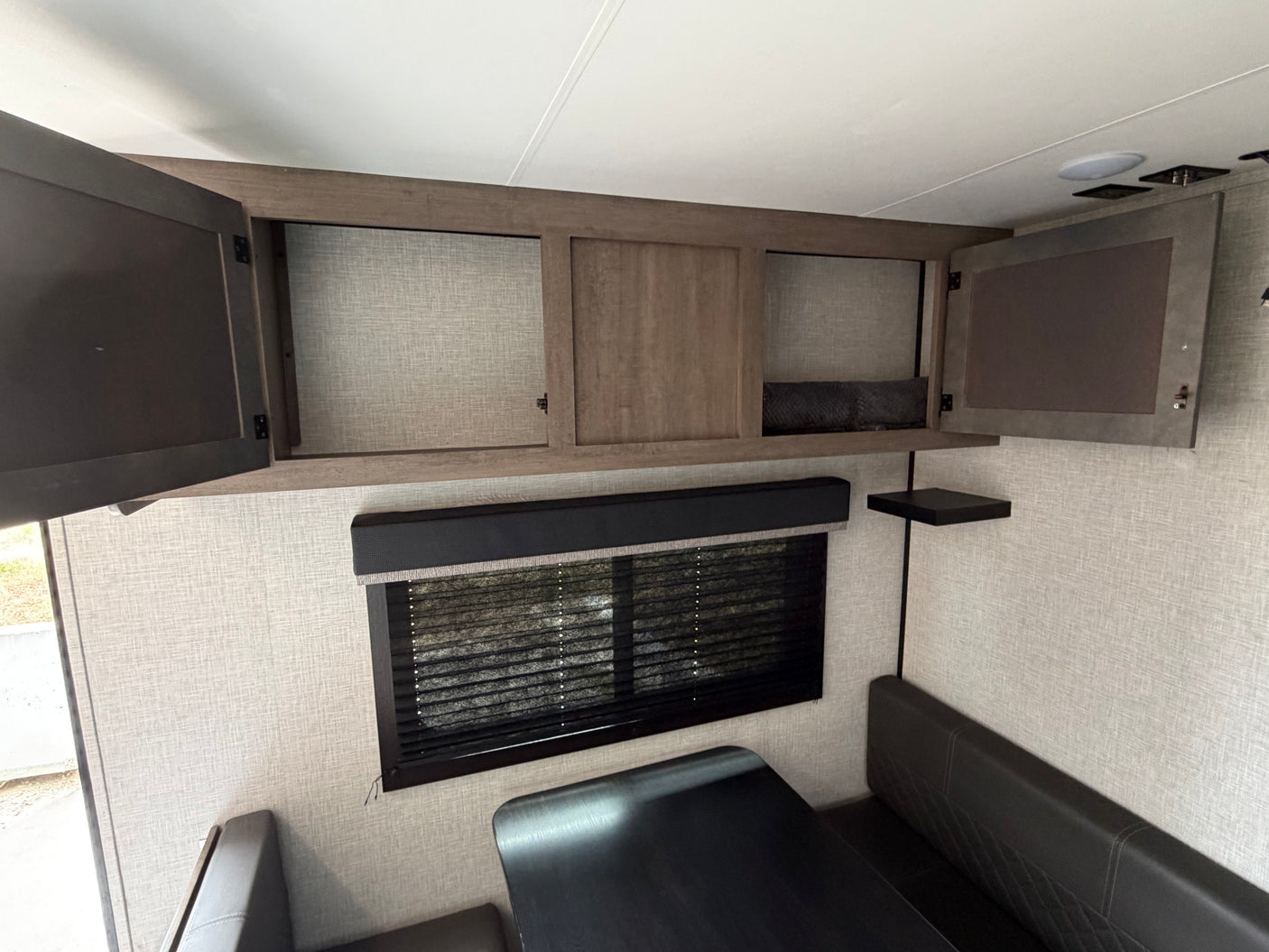 Modern rv rental interior showing open overhead storage cabinets, a dinette booth, and window blinds.