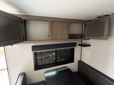 Modern rv rental interior showing open overhead storage cabinets, a dinette booth, and window blinds.