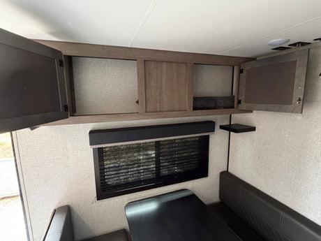 Modern rv rental interior showing open overhead storage cabinets, a dinette booth, and window blinds.