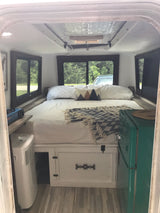 Compact rv rental interior with bed, portable AC, stove, and a retro green fridge, ideal for road trips and camping.