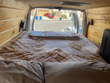 RV rental: View from a bed inside a wood-paneled camper van, looking out to a residential street with a red truck.