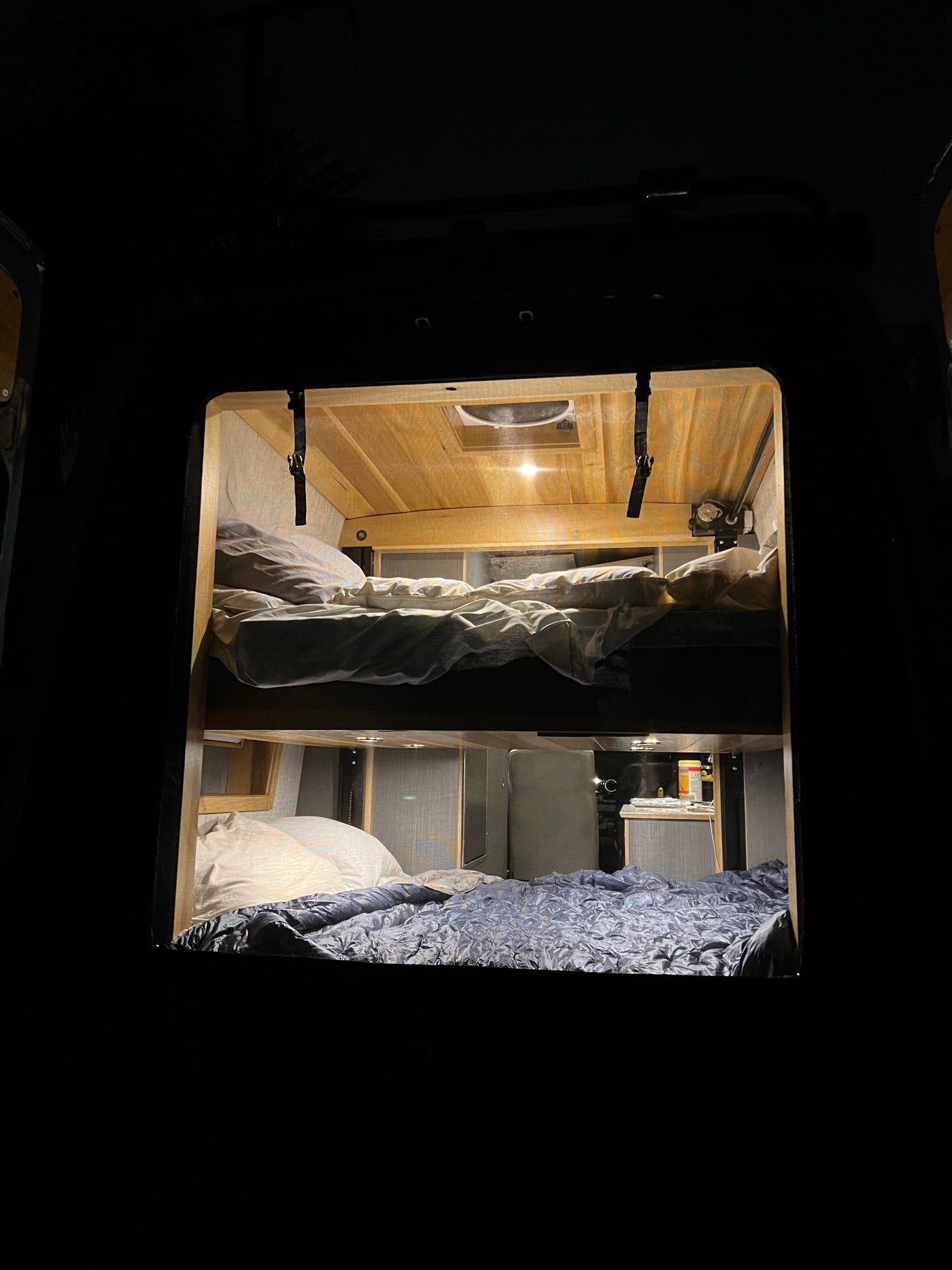 Inside a dark **rv rental**, warm light reveals cozy bunk beds with pillows & blankets. Wooden ceiling & subtle interior details are visible. — photo 7