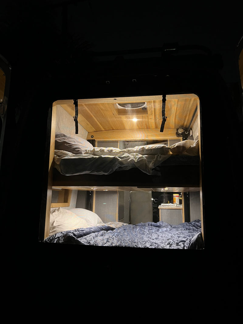 Inside a dark **rv rental**, warm light reveals cozy bunk beds with pillows & blankets. Wooden ceiling & subtle interior details are visible. — photo 7