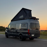 Dark grey Mercedes-Benz Sprinter camper van with a raised pop-top roof, ideal for an rv rental adventure under a sunset sky.