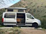 Silver camper van with pop-top open, showing interior kitchen. An RV rental parked by a hillside, ready for travel.