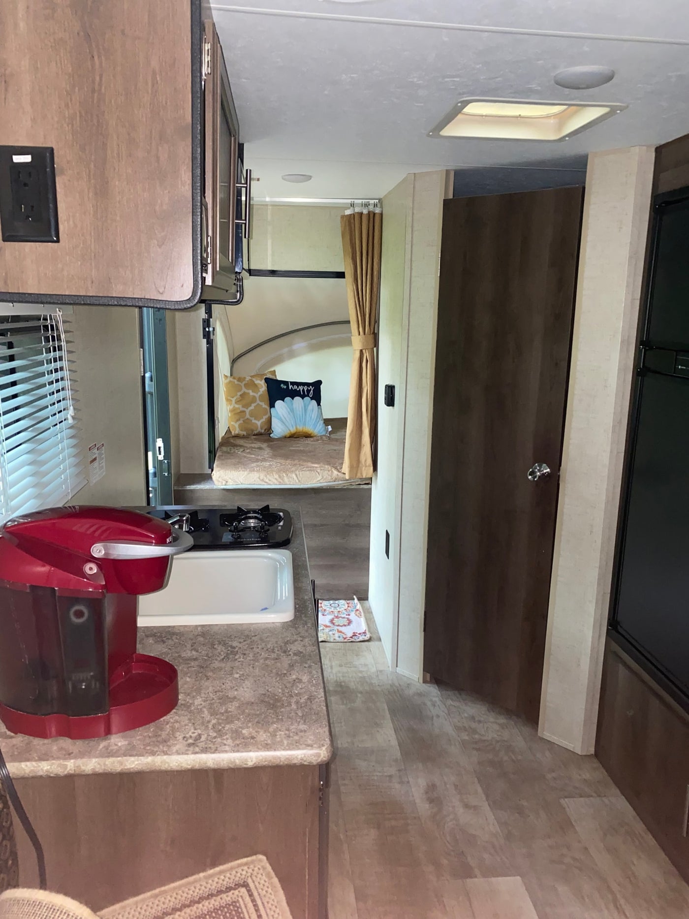 Inside an RV rental: a compact kitchen with sink, stovetop, and red coffee maker, leading to bunk beds in the back. — photo 2