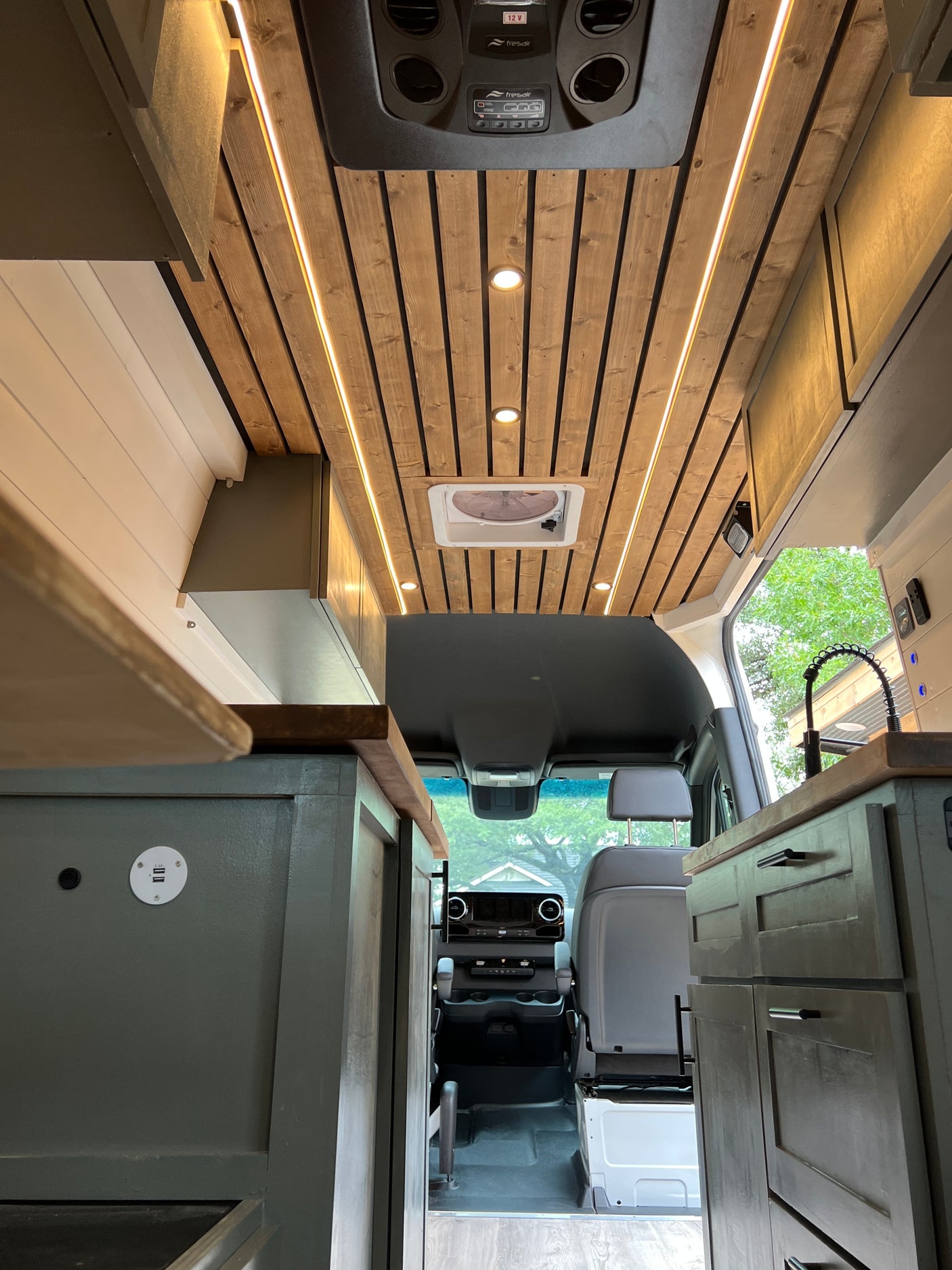 Inside a modern **rv rental** camper van: wooden ceiling, accent lighting, full kitchen, and clear view to the front cabin.