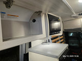 An rv rental's organized kitchen space, showing a Contoure microwave, overhead storage with USB charging, and light grey countertop.