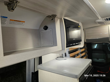An rv rental's organized kitchen space, showing a Contoure microwave, overhead storage with USB charging, and light grey countertop.