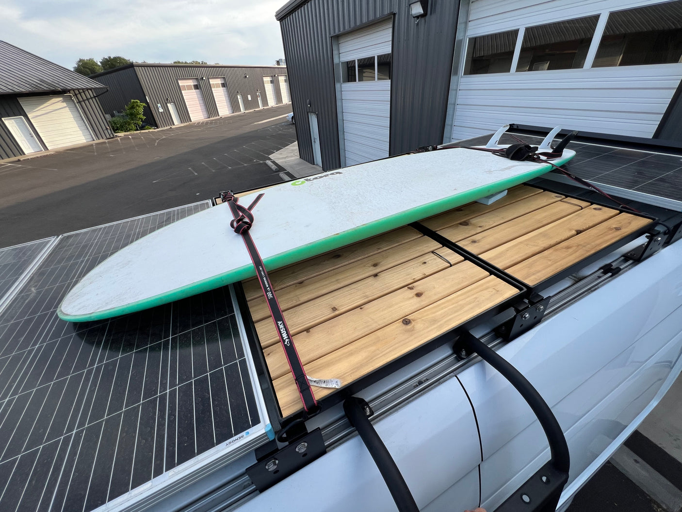 RV rental featuring rooftop solar panels, a wooden deck, and a surfboard secured on the roof rack.