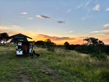 Peaceful RV rental camping at sunset. Person relaxes by a camper with a rooftop tent in a scenic, grassy landscape.