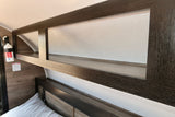 Inside an RV rental, a cozy sleeping area features built-in wood overhead storage shelves and essential safety equipment.