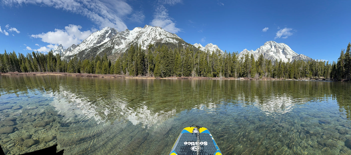 Panoramic mountain lake with clear water, snow peaks, and trees reflecting. Forefront paddleboard. Perfect for an RV rental trip!