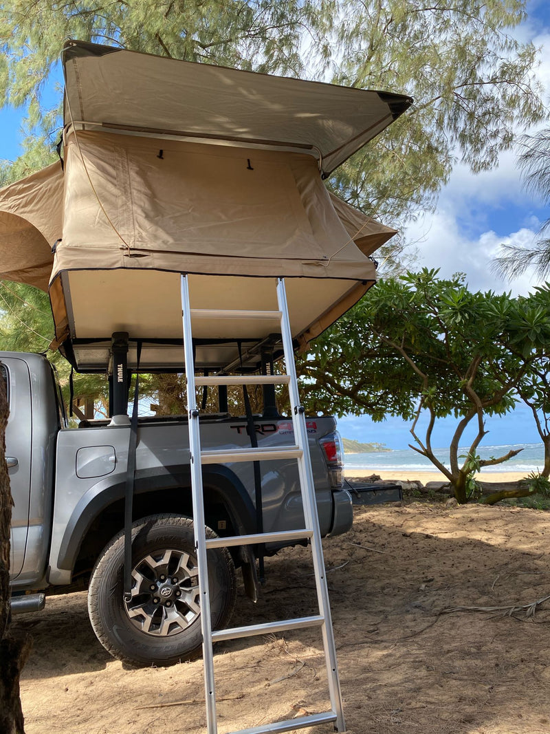 Grey Toyota Tacoma with a tan rooftop tent and ladder, parked on a sandy beach near the ocean. Great for RV rental adventures. — photo 3