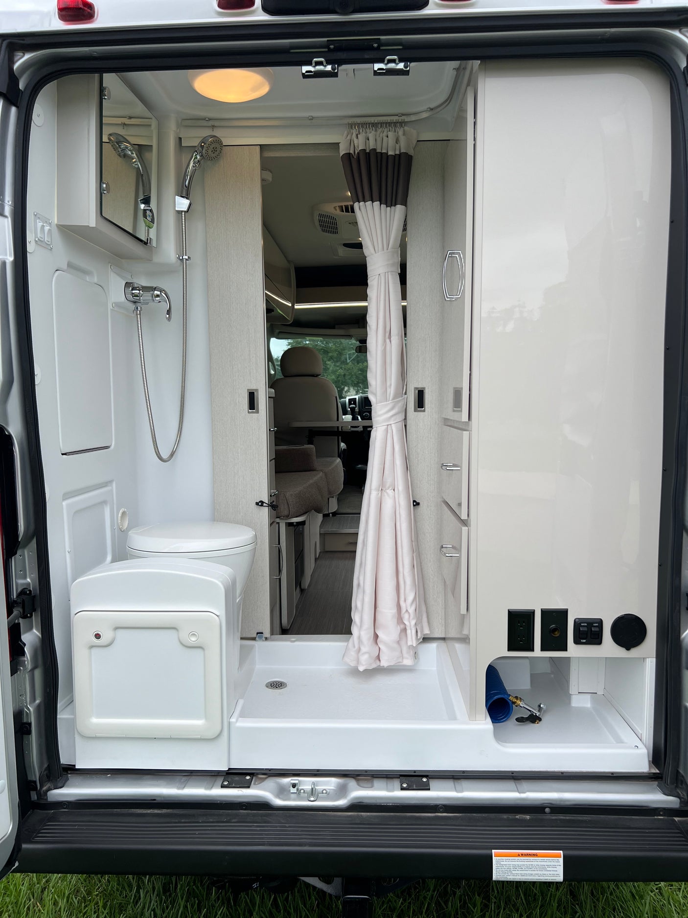 **RV rental** interior: Compact van bathroom featuring a shower, toilet, and utility connections at the rear of the camper.
