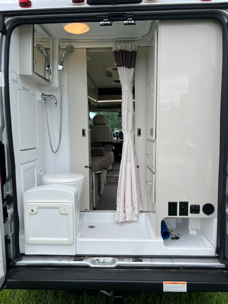**RV rental** interior: Compact van bathroom featuring a shower, toilet, and utility connections at the rear of the camper.