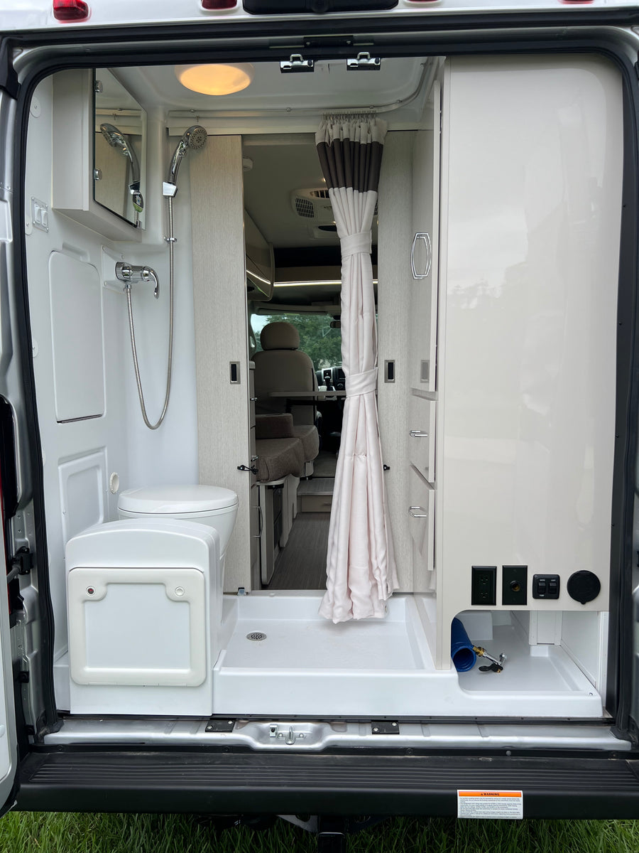 **RV rental** interior: Compact van bathroom featuring a shower, toilet, and utility connections at the rear of the camper.