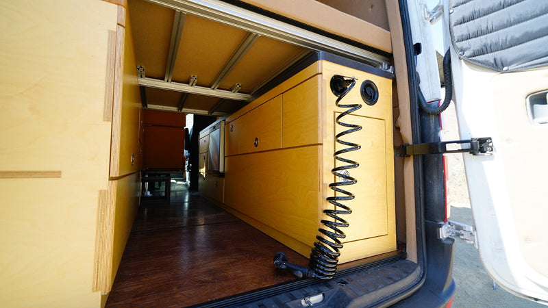 RV rental: Camper van's wood interior features custom storage cabinets, rugged flooring, and a rear utility/shower system. — photo 6