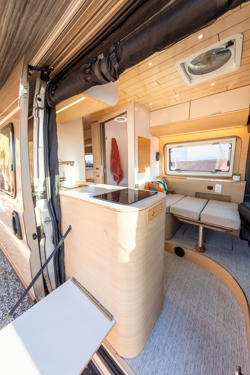  showcasing a compact kitchen and versatile dining area within a camper van.|RV rental camper van with extended awning and open door showing modern interior — photo 3
