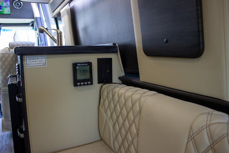 RV rental interior: Compact kitchen, thermostat (130°F), power outlet, and a cream-colored quilted seat with safety warning.