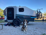 Your next rv rental adventure: A dog with a CampINawe teardrop camper & bikes at a gravel campsite.
