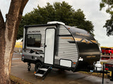 A Forest River Aurora Light travel trailer, ideal for an rv rental, parked on pavement with trees and an overcast sky.