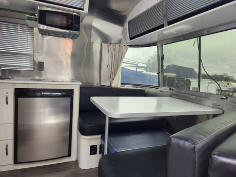 This RV rental's interior shows a polished aluminum kitchen with microwave, fridge, and dining area with black leather seating.
