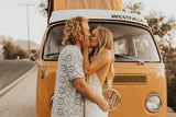 A loving couple kisses by their orange VW Westfalia camper van, perfect for an RV rental road trip adventure!