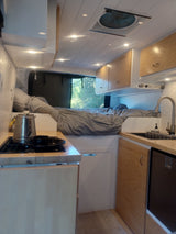 Cozy rv rental interior with kitchen, bed, and natural light. Perfect camper van for your next adventure.