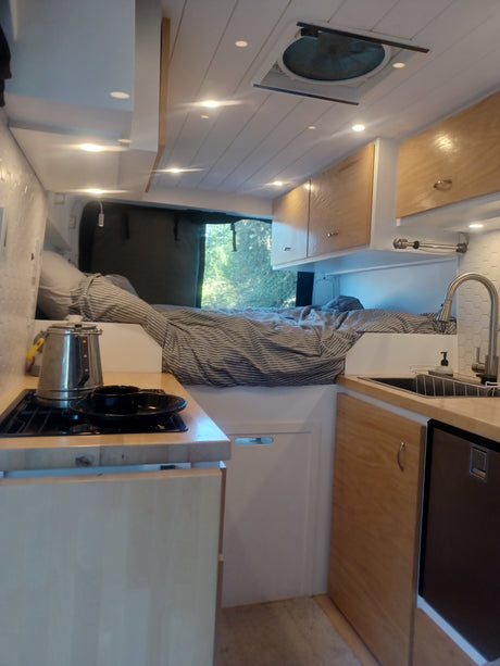 Cozy rv rental interior with kitchen, bed, and natural light. Perfect camper van for your next adventure.